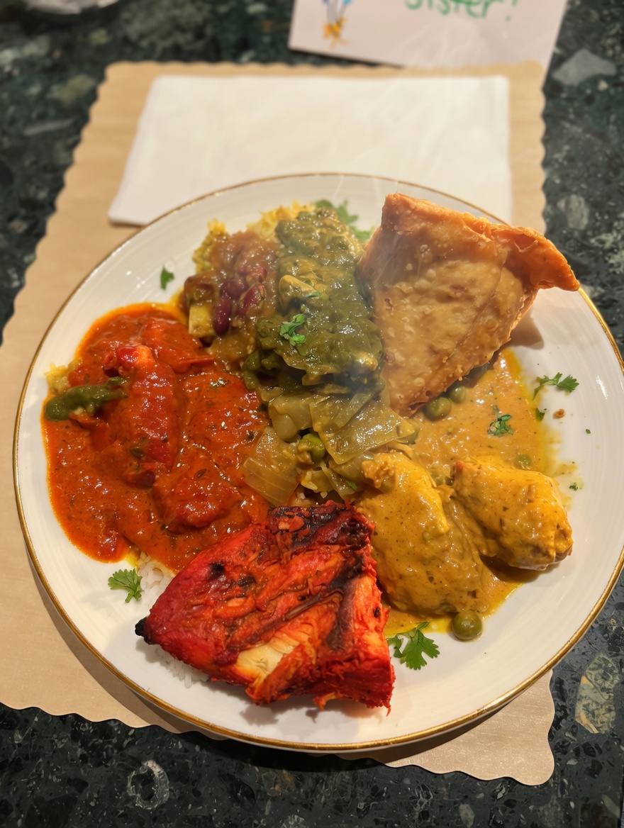 Appetizing plated selection from the New Delhi Indian Restaurant buffet featuring a variety of curries, vegetable samosa, tandoori chicken, rice, and vegetables on elegant dishware